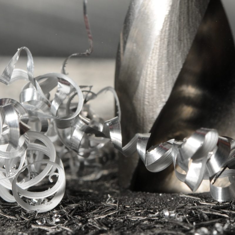 Closeup photo of hole drilling process, metal shavings around drill. Blurred background